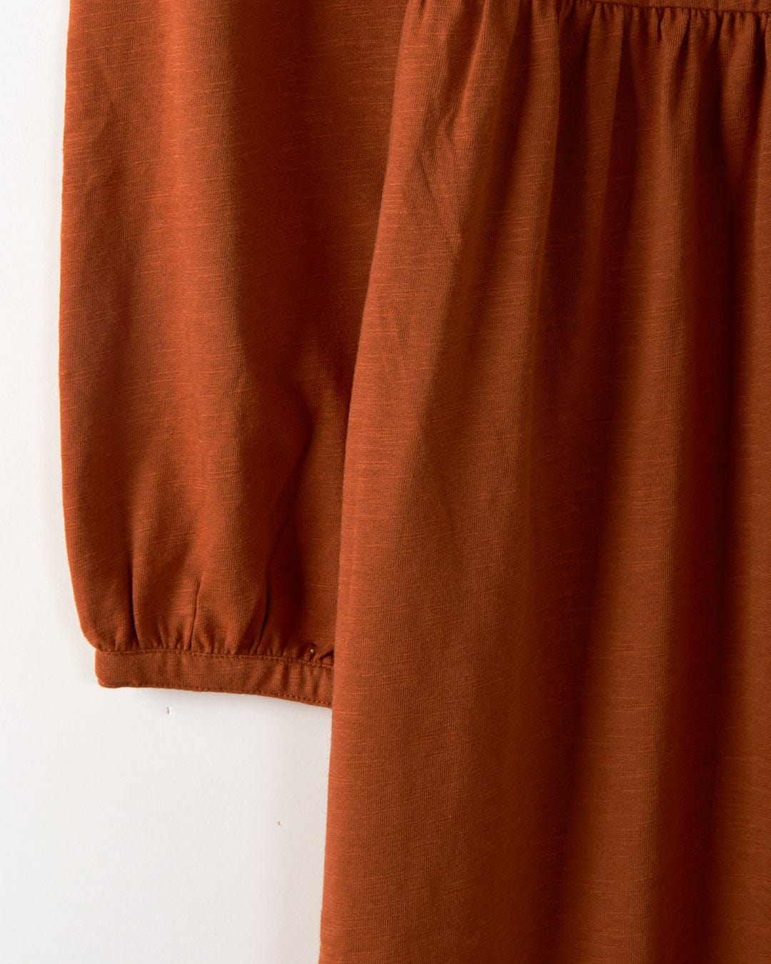 A close-up reveals the flowing texture and gathered sleeve of the Winnie women's dress in dark orange, crafted by Saltrock in a soft jersey slub fabric.