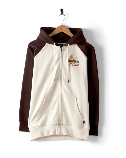 The Winter Poster Women's Cream Zip Raglan Hoodie by Saltrock features an embroidered abstract design of waves, a sun, and mountains, made from recycled polyester. This stylish piece reflects Saltrock's nature-inspired aesthetics.