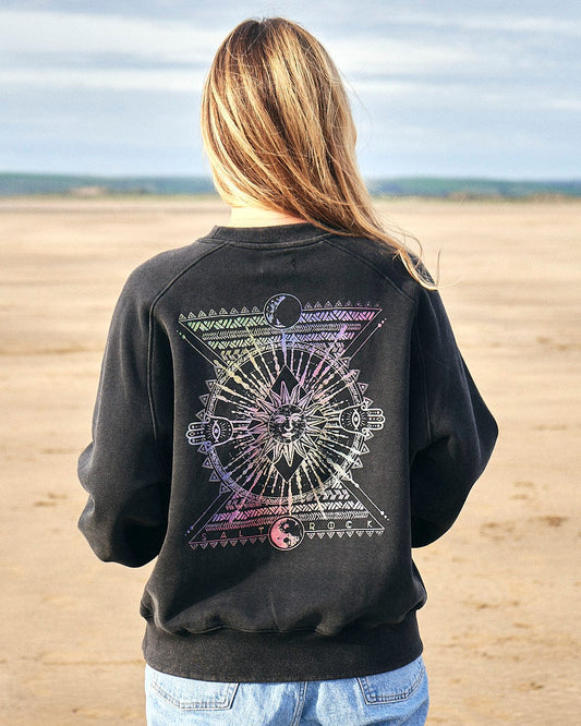 A woman wearing a Saltrock Winter Solstice Gradient - Womens Sweat - Washed Black sweatshirt standing on the beach during winter.