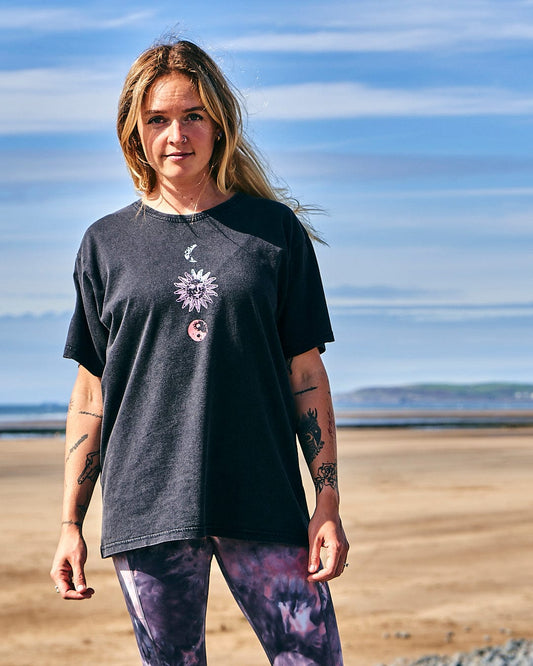 A woman wearing a Saltrock Winter Solstice Gradient - Womens Short Sleeve T-Shirt - Washed Black and leggings standing on the beach.