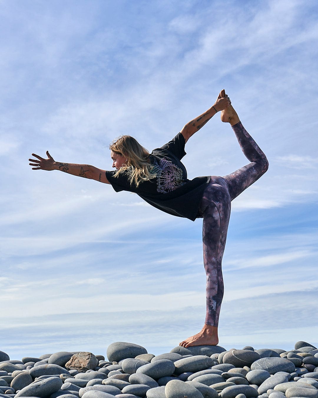 A woman doing a yoga pose on rocks wearing a crew neck Winter Solstice Gradient tee made of 100% cotton, by Saltrock.
