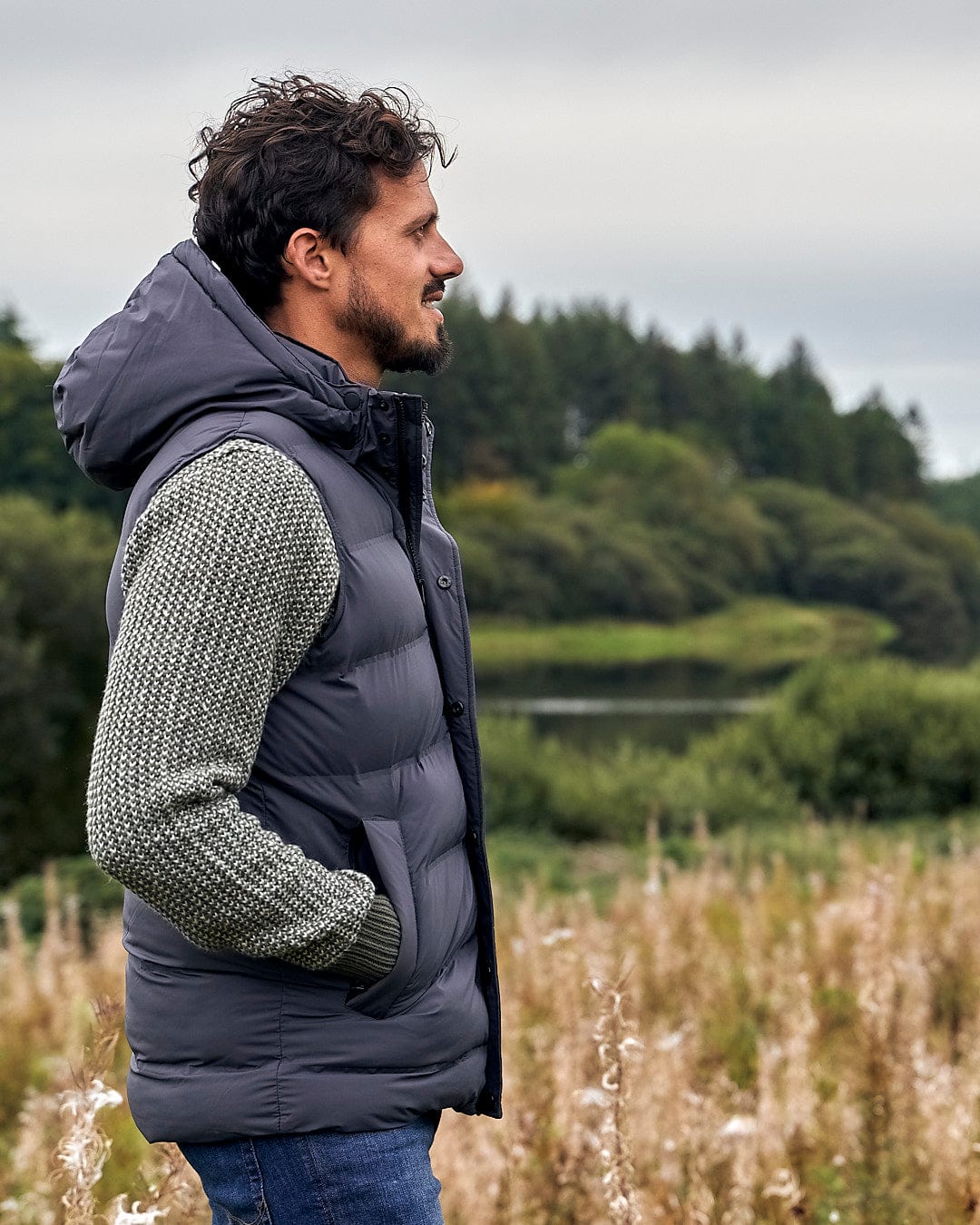 A man standing in a water-resistant field with a Saltrock Xavier - Mens Padded Gilet - Dark Grey.