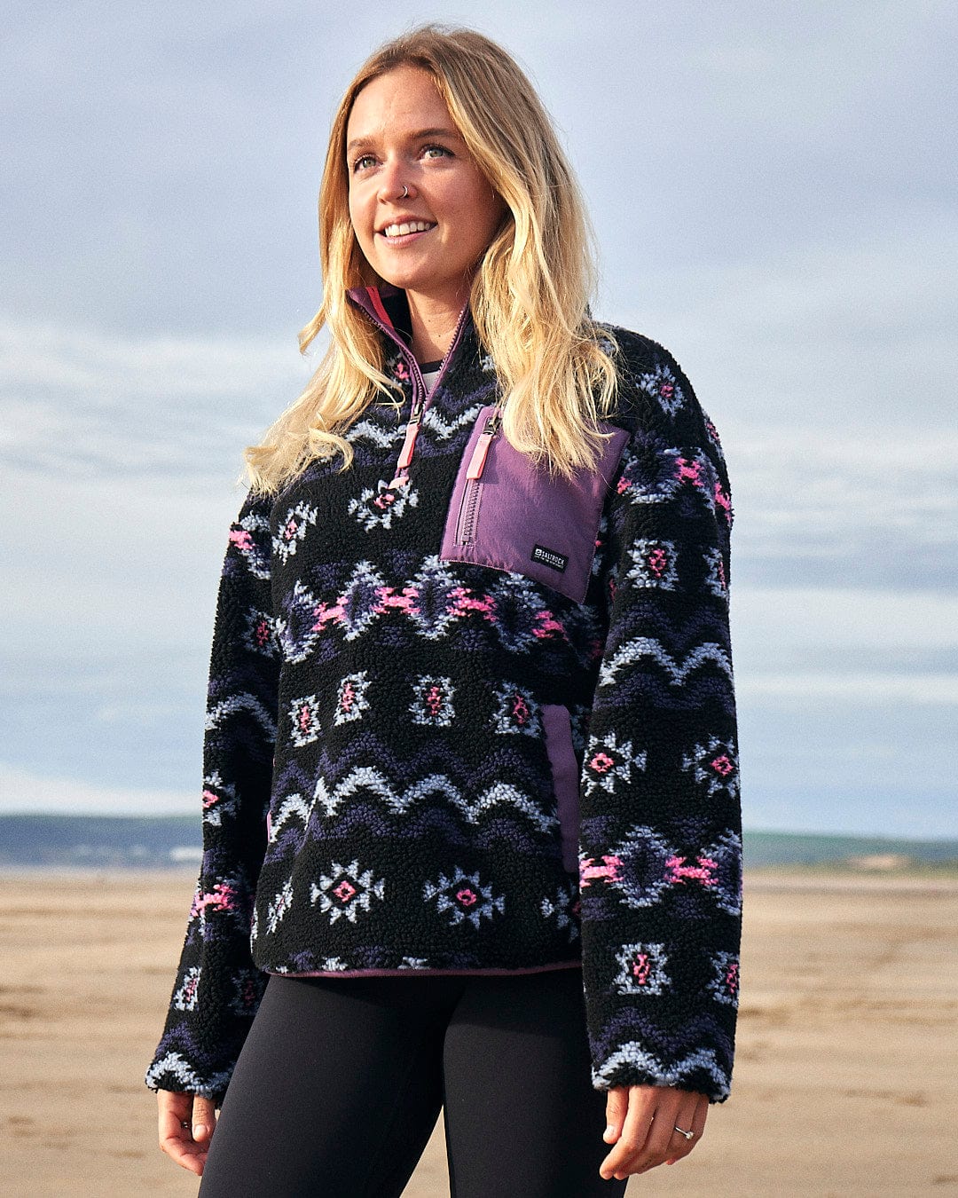 A woman is standing on the beach wearing a Saltrock Zella - Womens 1/4 Neck Fleece - Black pullover.