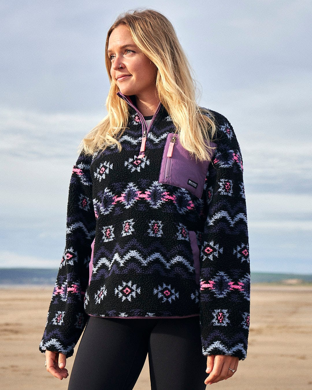A woman is standing on the beach wearing a Saltrock - Zella Womens 1/4 Neck Fleece in Black and pink.