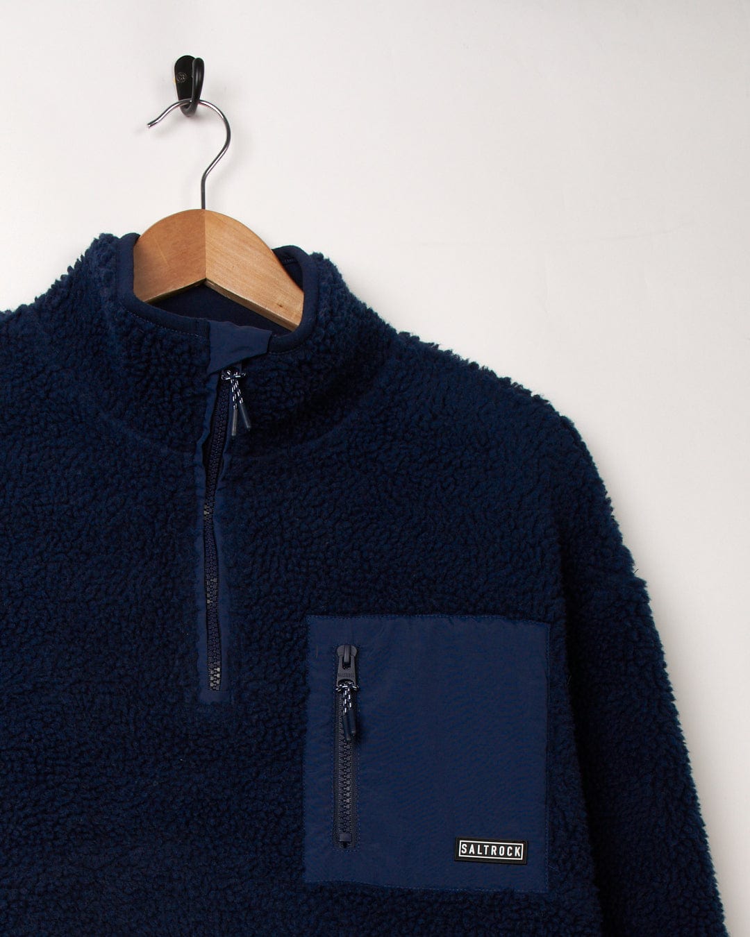 A cozy Saltrock Zella - Womens 1/4 Neck Fleece - Dark Blue pullover with a pocket, hanging on a hanger.