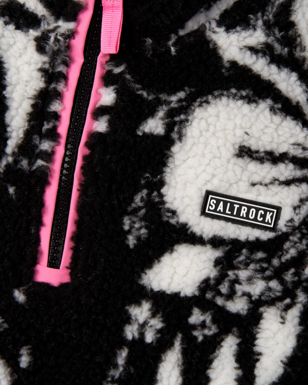 Close-up of a cosy Zella - Kids Hibiscus Fleece - Black with a floral hibiscus print, featuring a pink zipper and a Saltrock brand label.