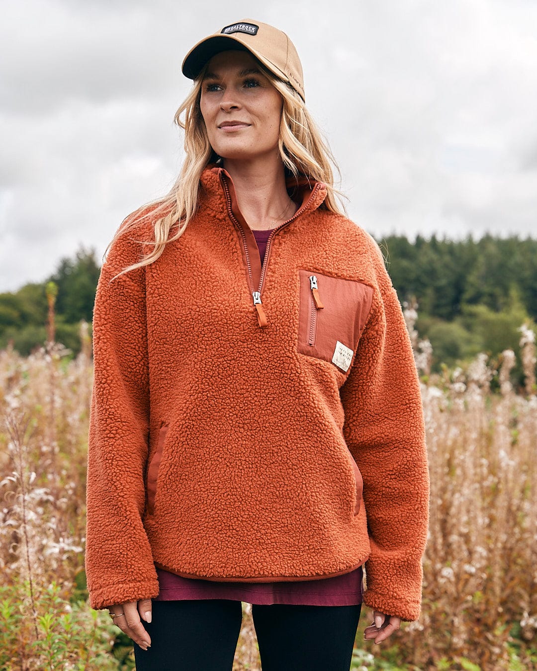 A woman is standing in a field wearing a Saltrock Zella Solid - Womens Borg Fleece - Burnt Orange pullover.