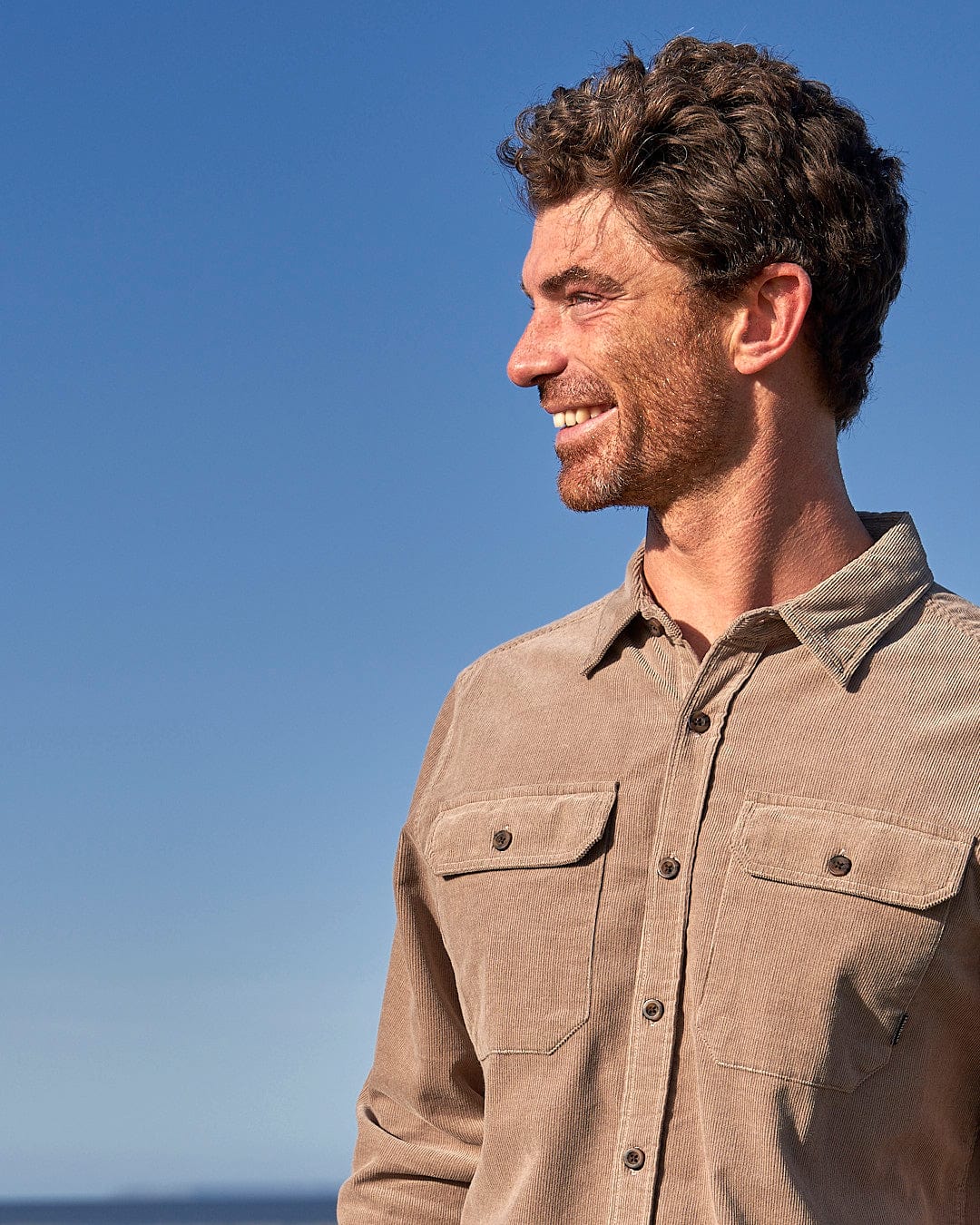 A man wearing a Saltrock Ace - Men Corduroy Shirt - Light Brown standing on the beach.