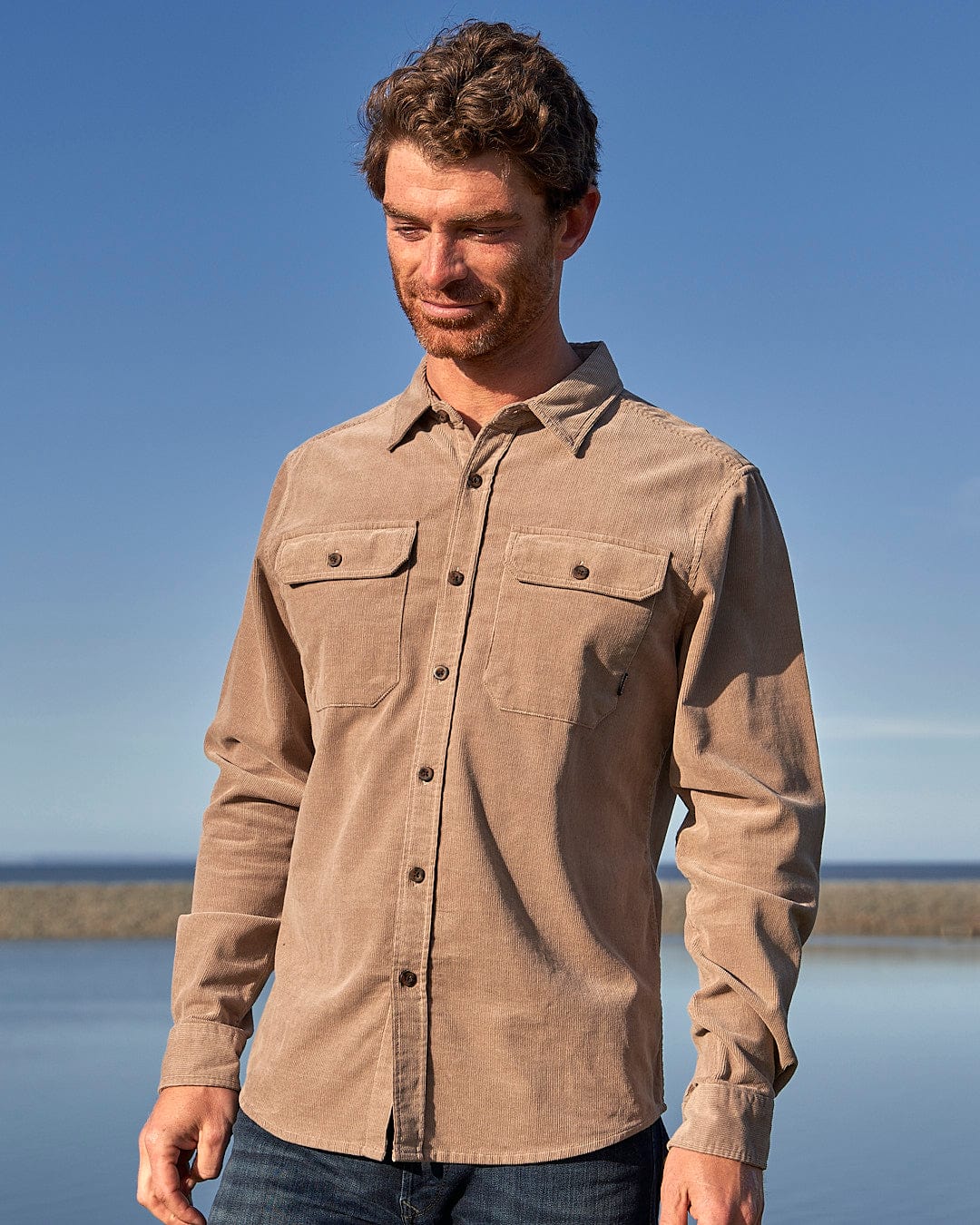 A man wearing a Saltrock Ace - Men Corduroy Shirt - Light Brown standing by the water.