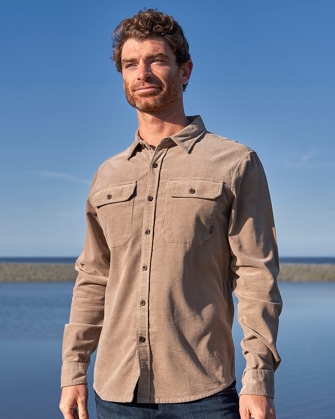 A man wearing a Saltrock - Ace Men Corduroy Shirt - Light Brown standing in front of a body of water.