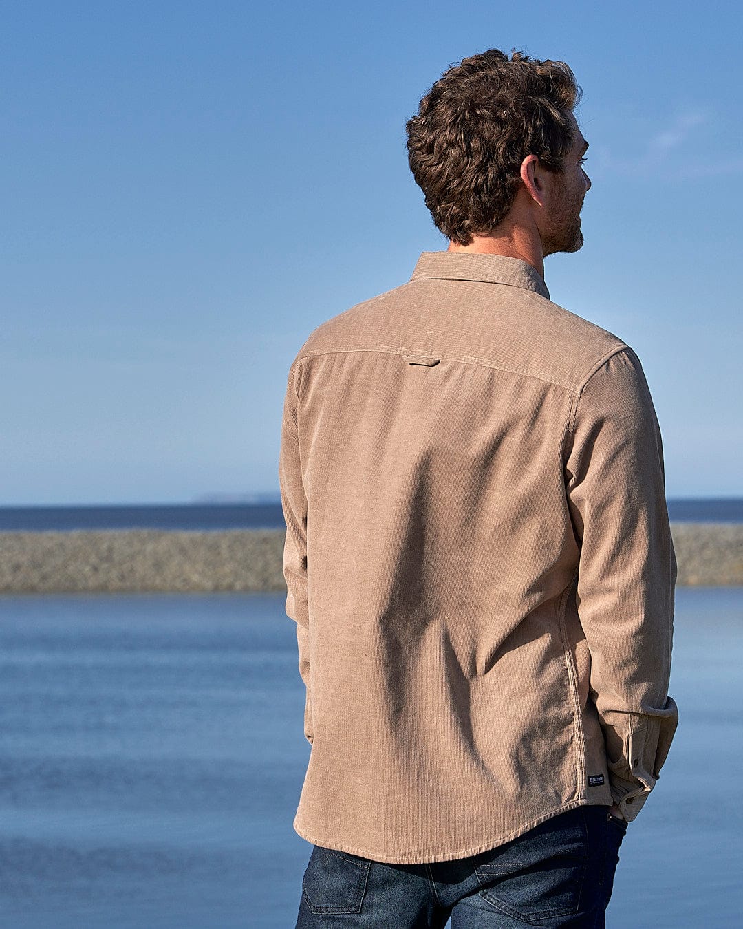 A man wearing a Saltrock - Ace Men Corduroy Shirt - Light Brown is standing by the water.