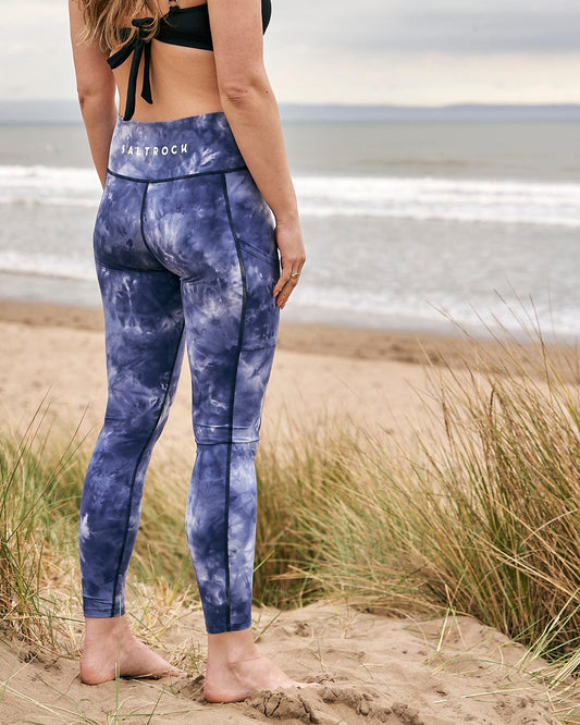 A woman standing on the beach in Saltrock Ahimsa - Womens Legging - Blue made of stretch material.
