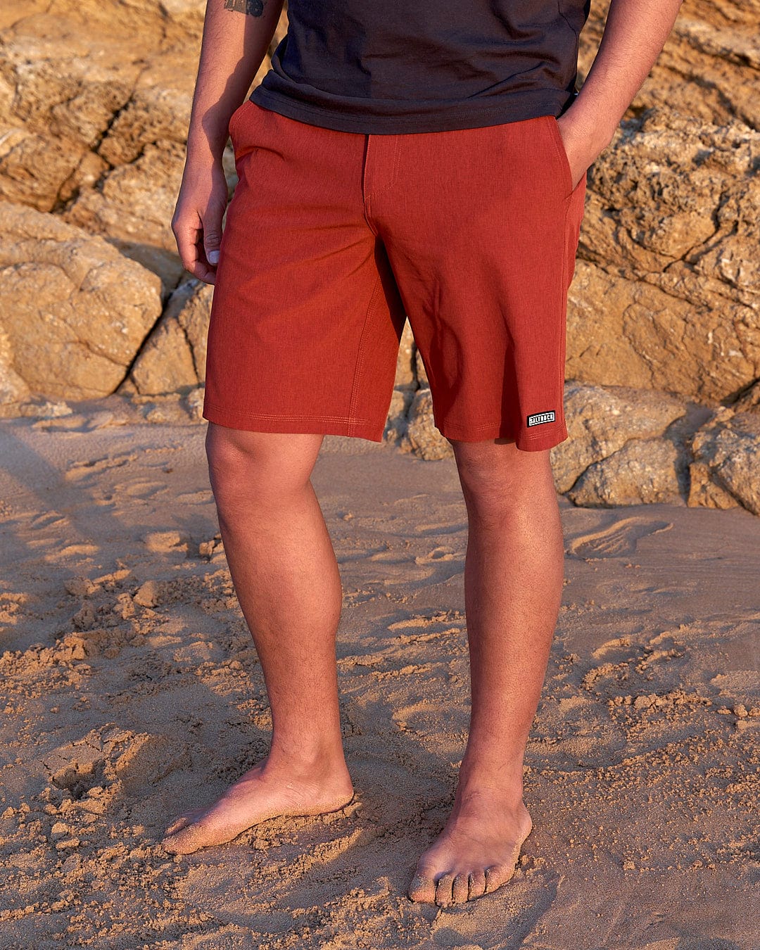 a man in Saltrock Amphibian II - Mens Boardshort - Red standing on a beach.