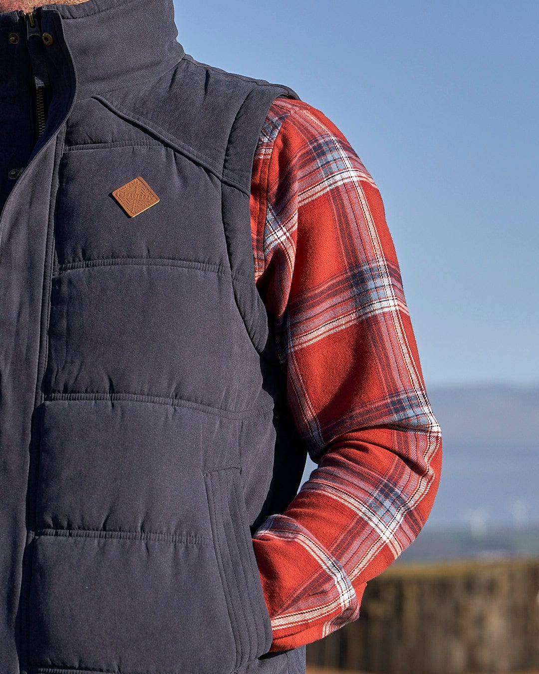 A man in a plaid shirt wearing a Saltrock Bardsey Mens Gilet in Blue.