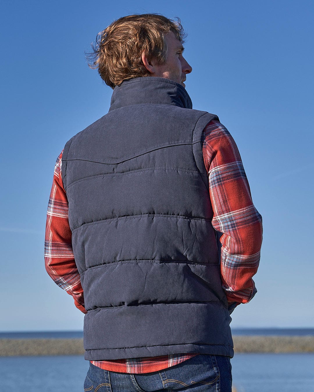 A man wearing a Saltrock Bardsey - Mens Gilet - Blue looking at the water.