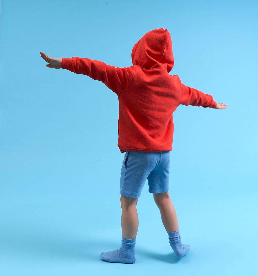 A young boy in a Saltrock Kids Pop Hoodie - Red standing on a blue background.