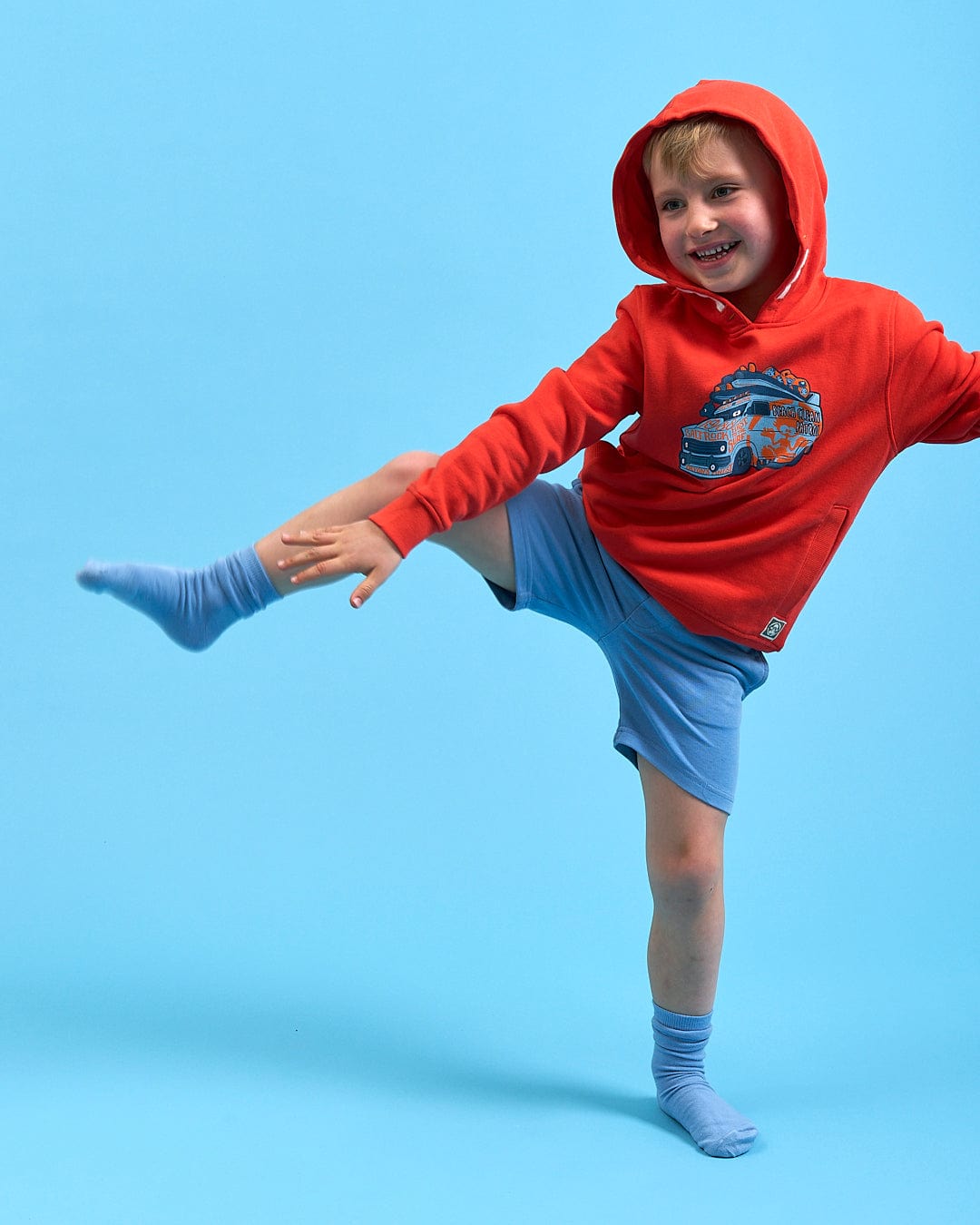 A young boy in a Saltrock Beach Patrol - Kids Pop Hoodie - Red and shorts doing a kick.