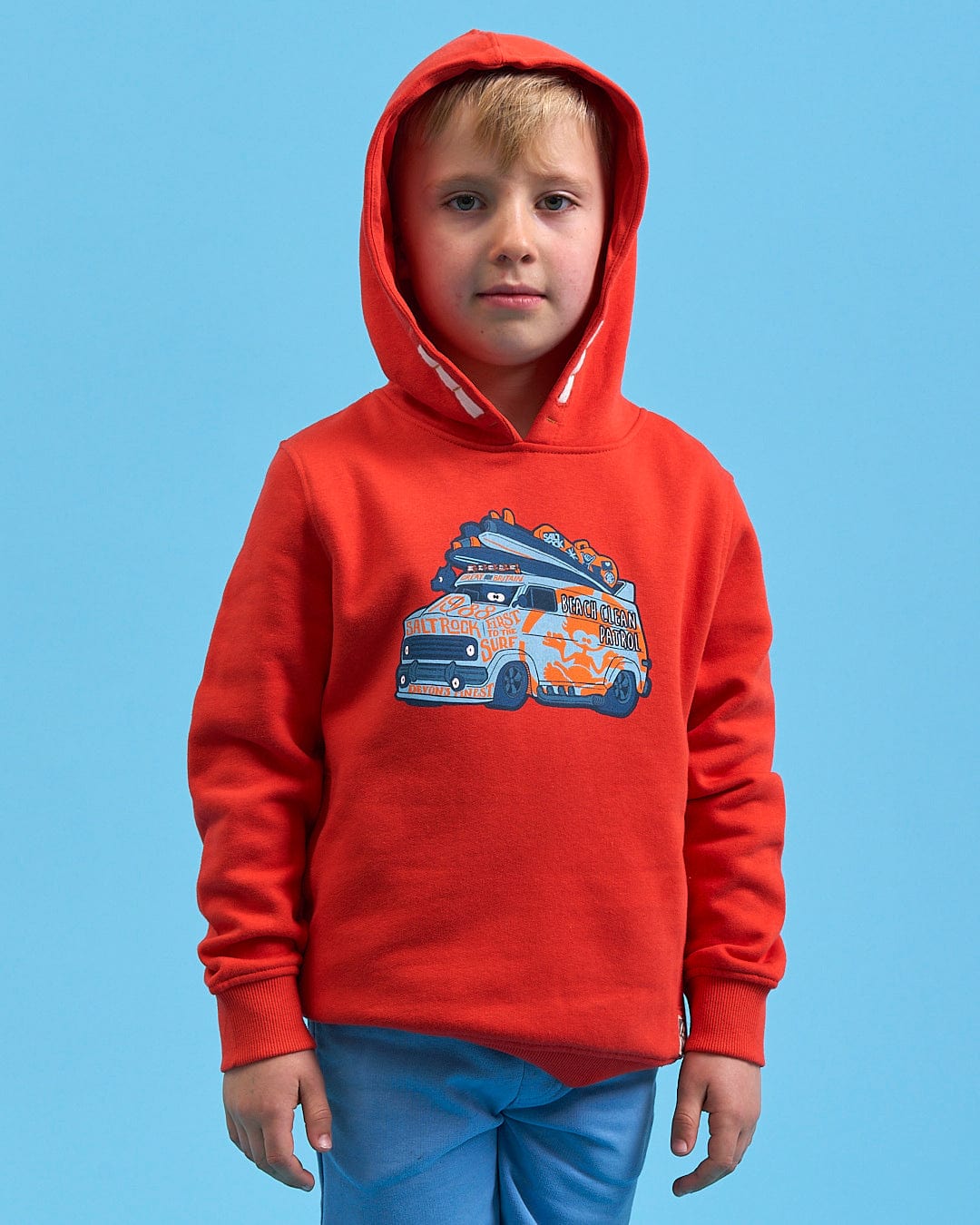 A young boy wearing a Saltrock Beach Patrol - Kids Pop Hoodie - Red with a van on it.