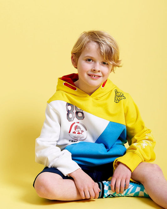 A young boy wearing a Bunny Hop - Kids Pop Hoodie - Yellow by Saltrock sitting on a yellow background.