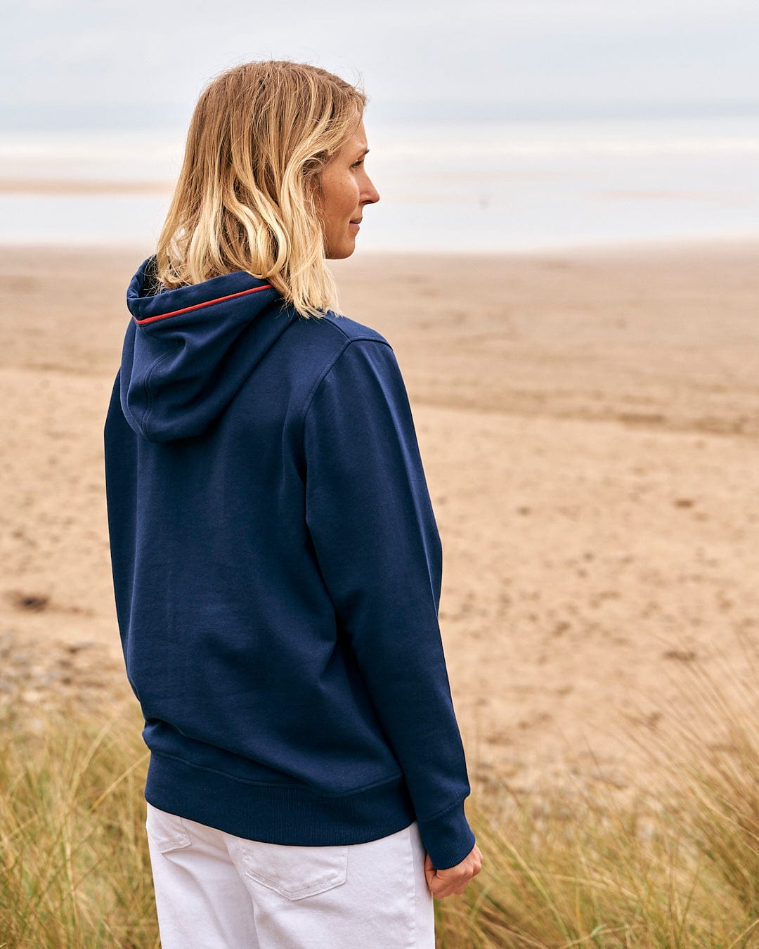 a woman wearing a Saltrock Celeste Pipe - Womens Pop Hoodie - Blue looking at the beach.