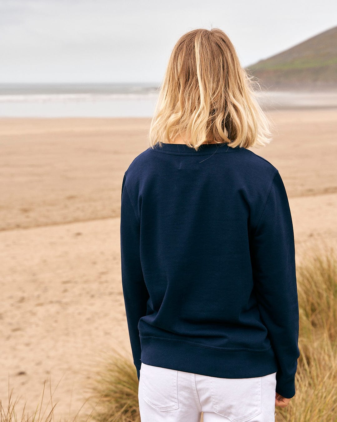 A woman standing on the beach wearing a Saltrock Celeste Stripe - Womens Crew Sweat - Blue sweatshirt.
