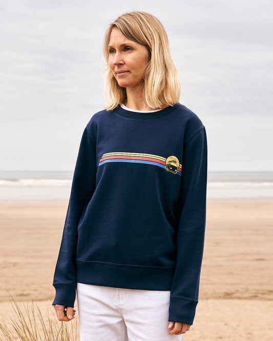 A woman standing on the beach wearing a Saltrock Celeste Stripe - Womens Crew Sweat - Blue.