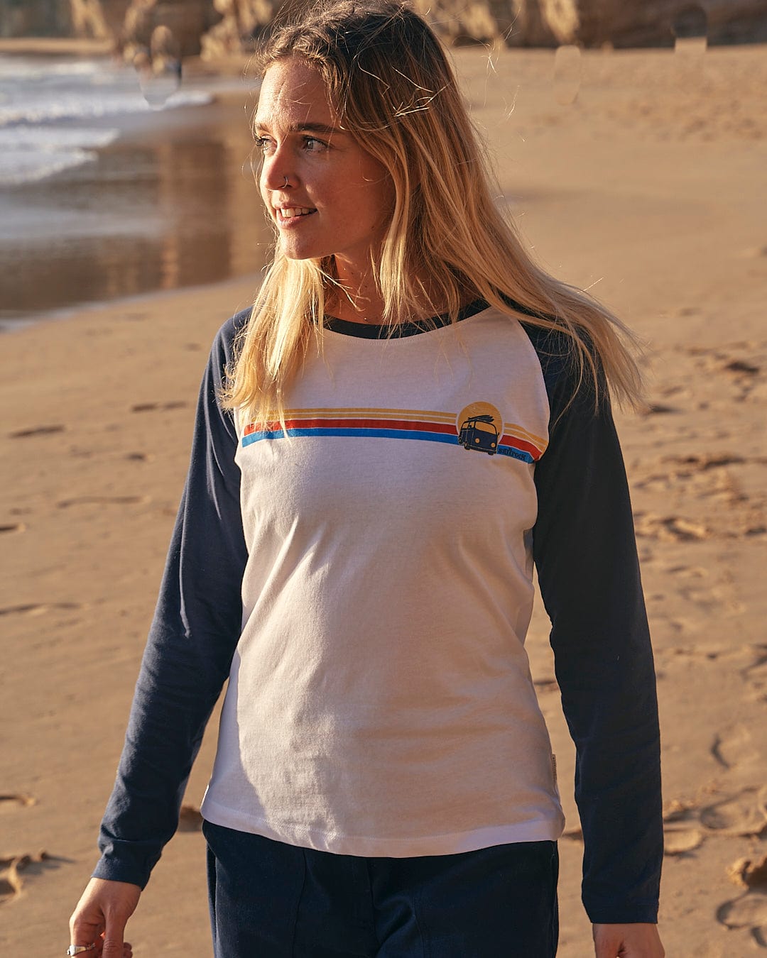 A woman walking on the beach wearing a Saltrock Celeste Stripe - Womens Long Sleeve Raglan T-Shirt in White/navy.