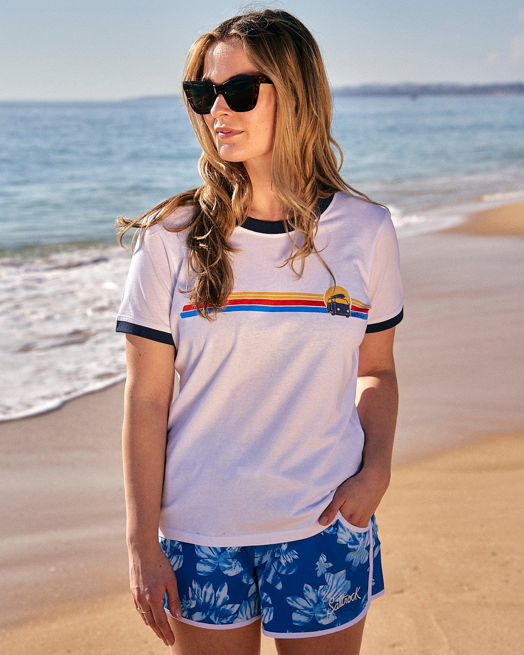A woman wearing a Saltrock Celeste Stripe - Womens Ringer Tee - White, standing on a beach.
