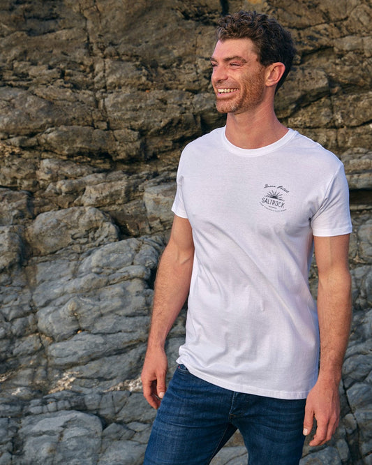 A man wearing a Dawn Patrol - Mens Short Sleeve T-Shirt - White by Saltrock in front of rocks.