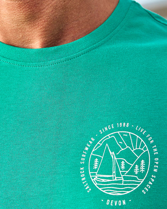 A man wearing a Saltrock Devon Sailaway Outline - Mens Short Sleeve T-Shirt - Bright Green with a boat on it.