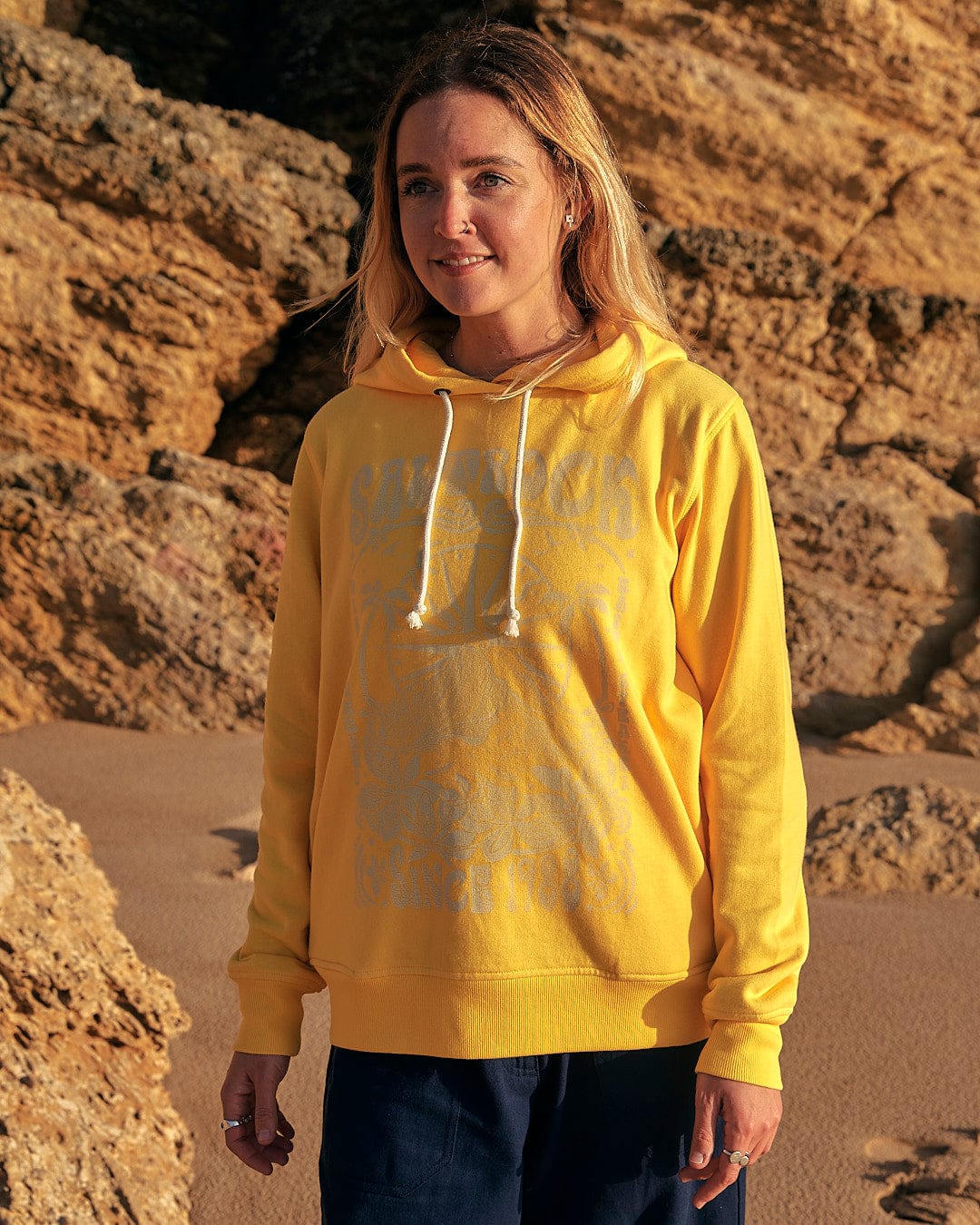A woman wearing a Saltrock Dreamseeker - Womens Pop Hoodie - Yellow standing on a beach.