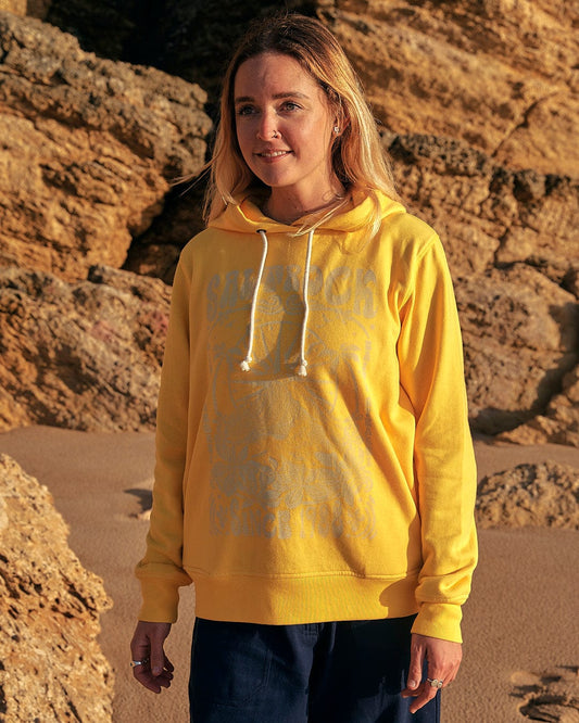 A woman wearing a Saltrock Dreamseeker - Womens Pop Hoodie - Yellow standing on a beach.