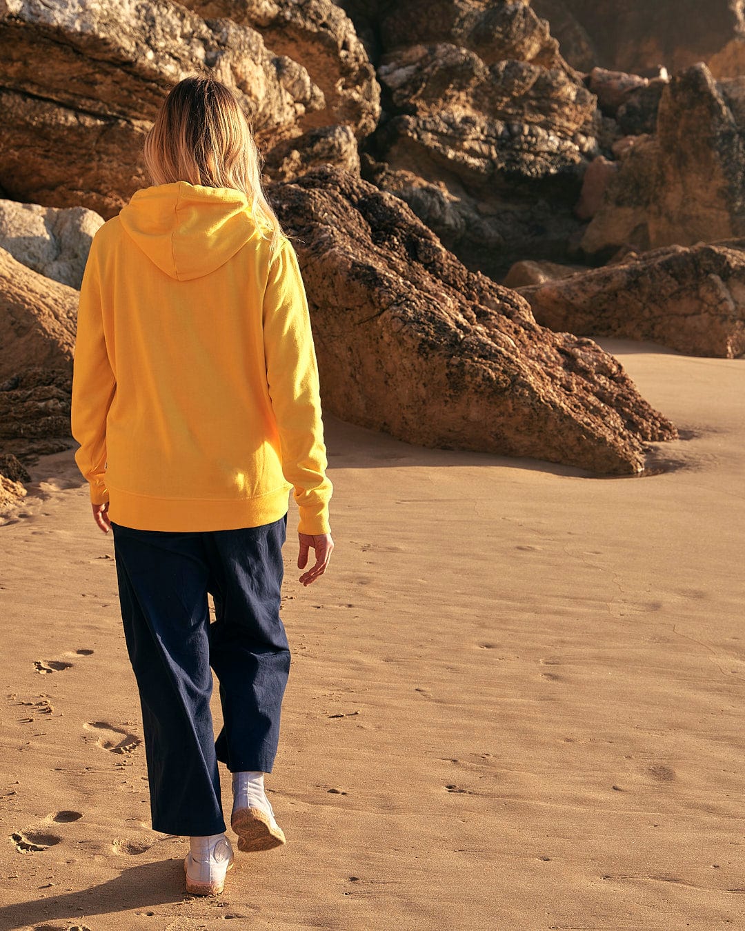 A woman wearing a Saltrock Dreamseeker - Womens Pop Hoodie - Yellow walking on the beach.