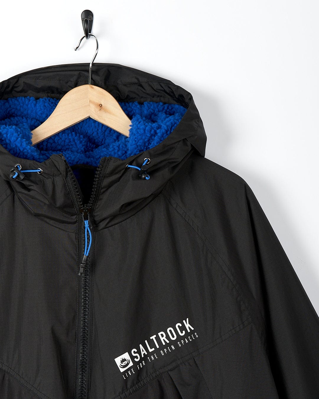 A Saltrock Four Seasons - Waterproof Changing Robe - Black/Blue with a blue hood hanging on a hanger.