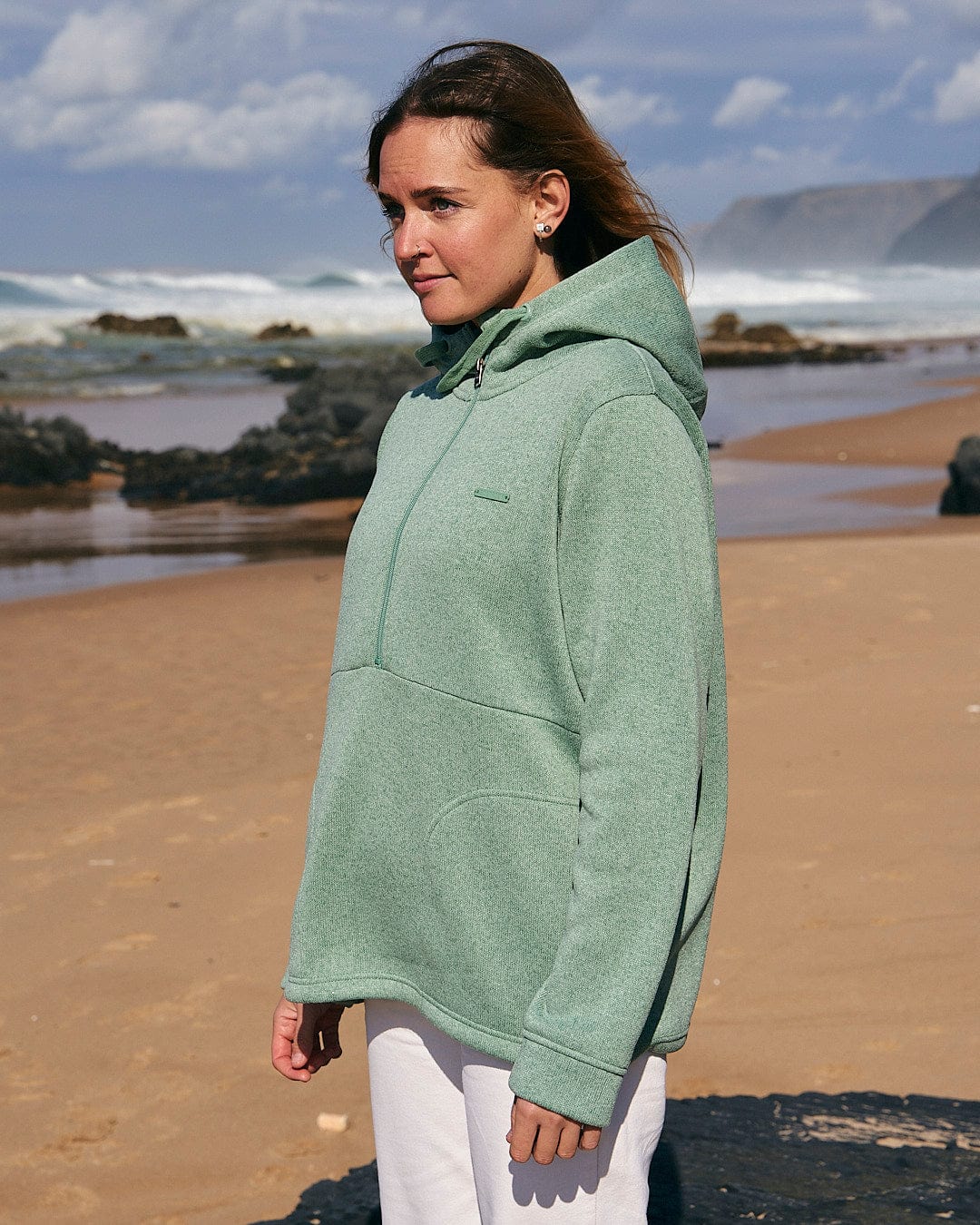 A woman standing on a beach wearing a Saltrock Galaksea - Womens 1/4 Zip Fleece - Light Green hoodie.