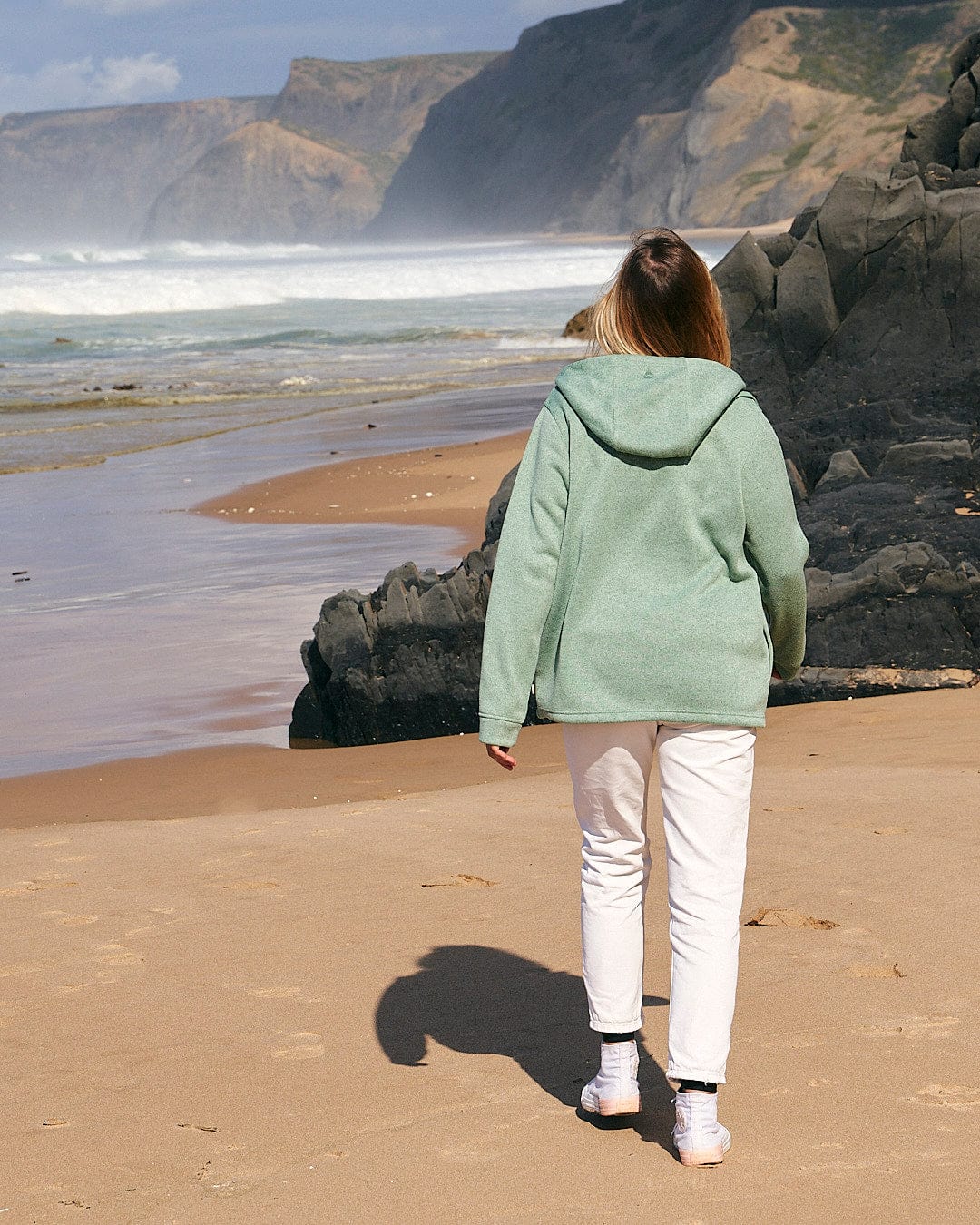 A woman walking on a beach near the ocean wearing the Saltrock Galaksea - Womens 1/4 Zip Fleece in Light Green.