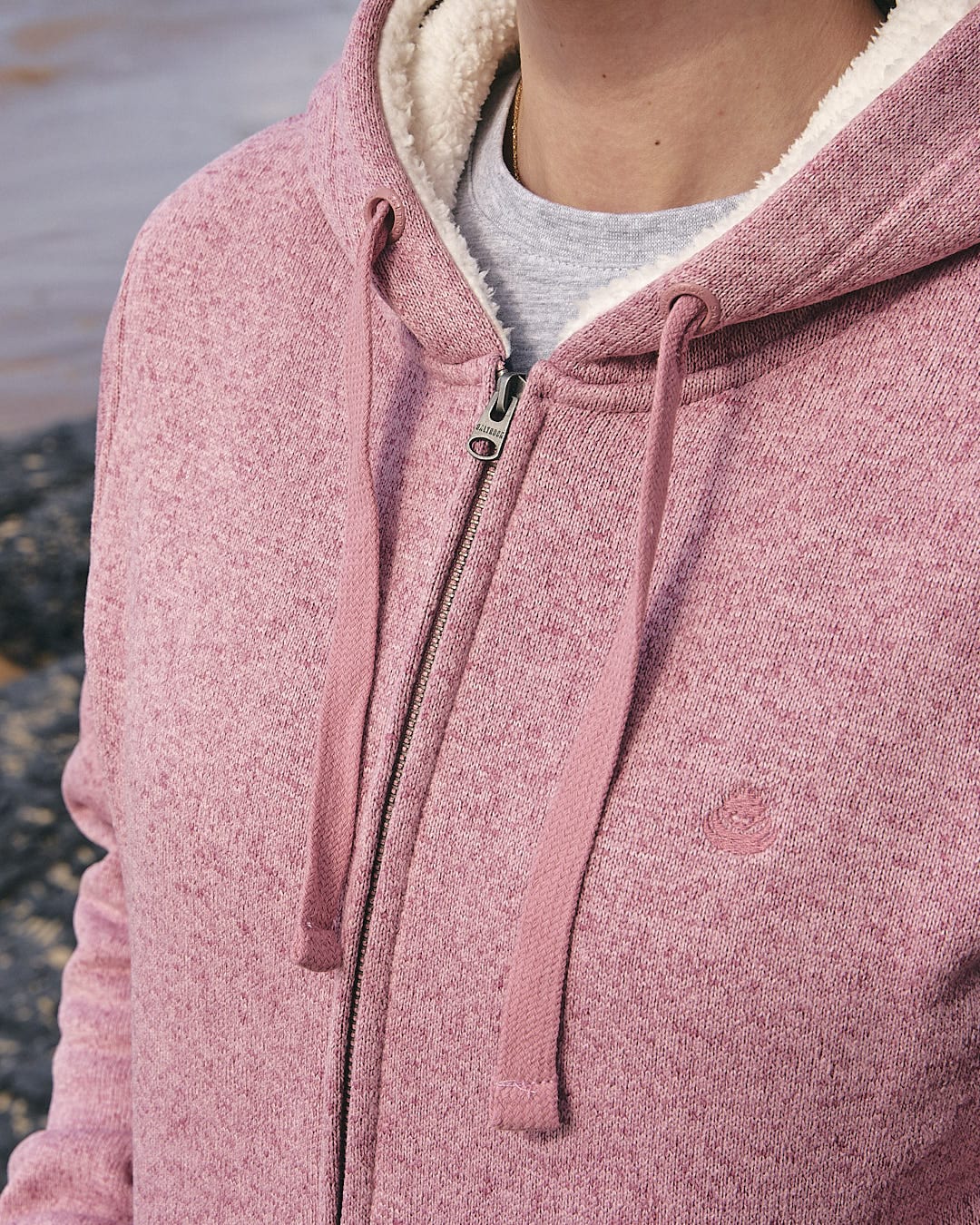 A woman wearing a comfortable Saltrock Galak - Womens Fur Lined Hoody - Pink on the beach.
