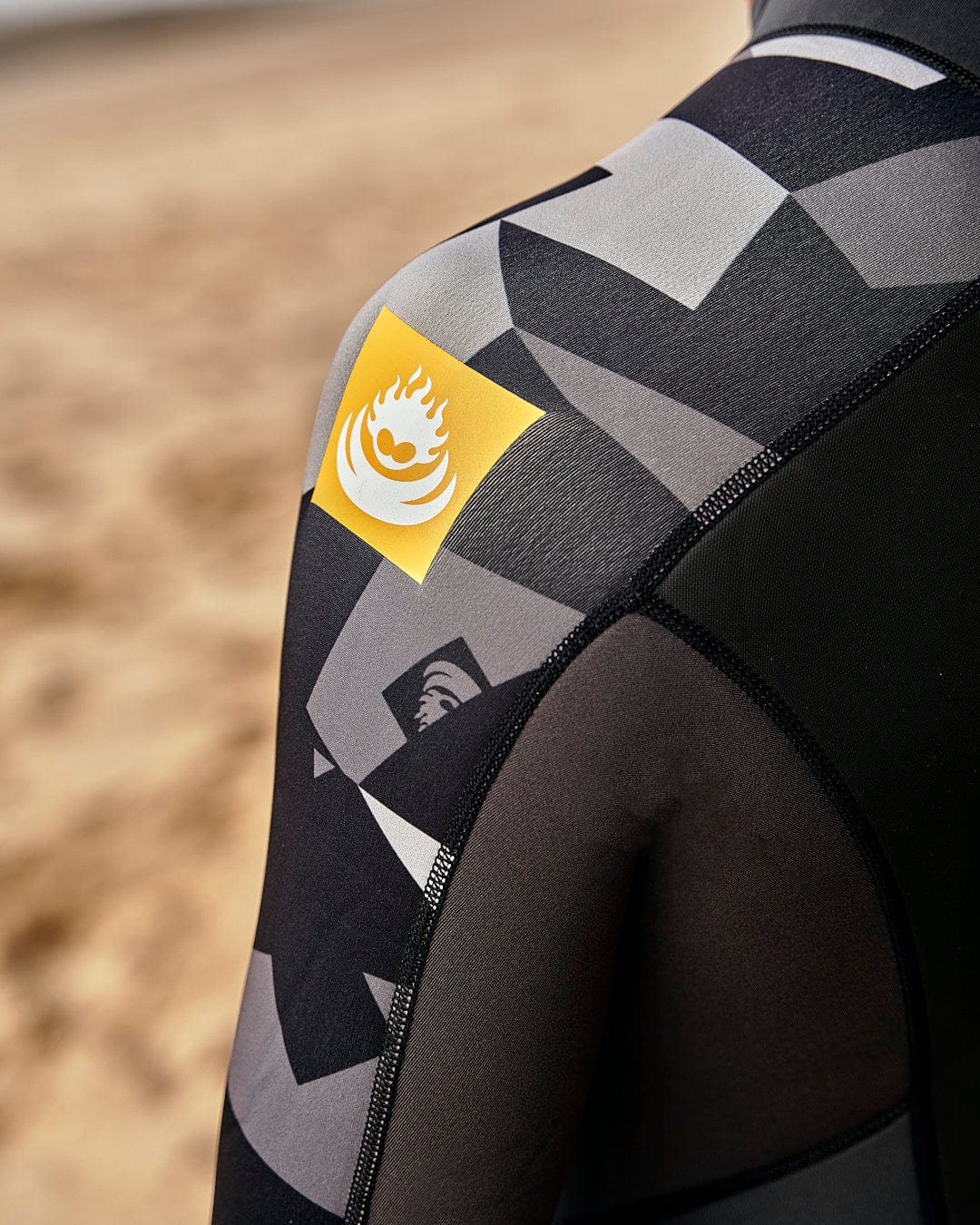 The back of a man wearing a Saltrock Geo Camo - Mens 3/2 Full Wetsuit - Black on the beach.