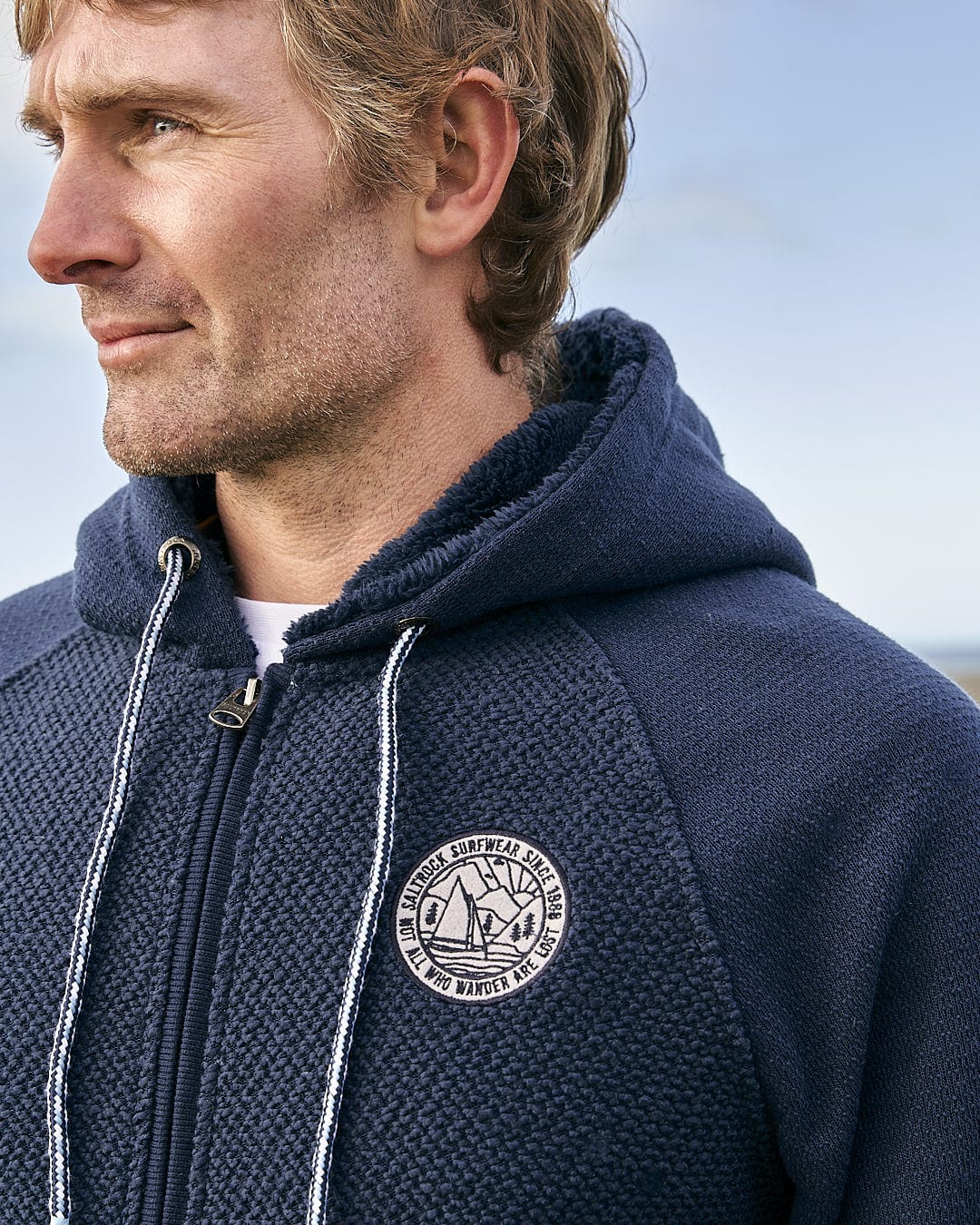 A man wearing a Saltrock - Hall Mens Orkney Borg Lined Hoodie - Dark Blue with a badge on it.