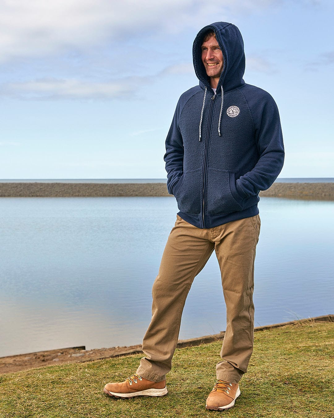 A man in a Saltrock hoodie standing next to a body of water.