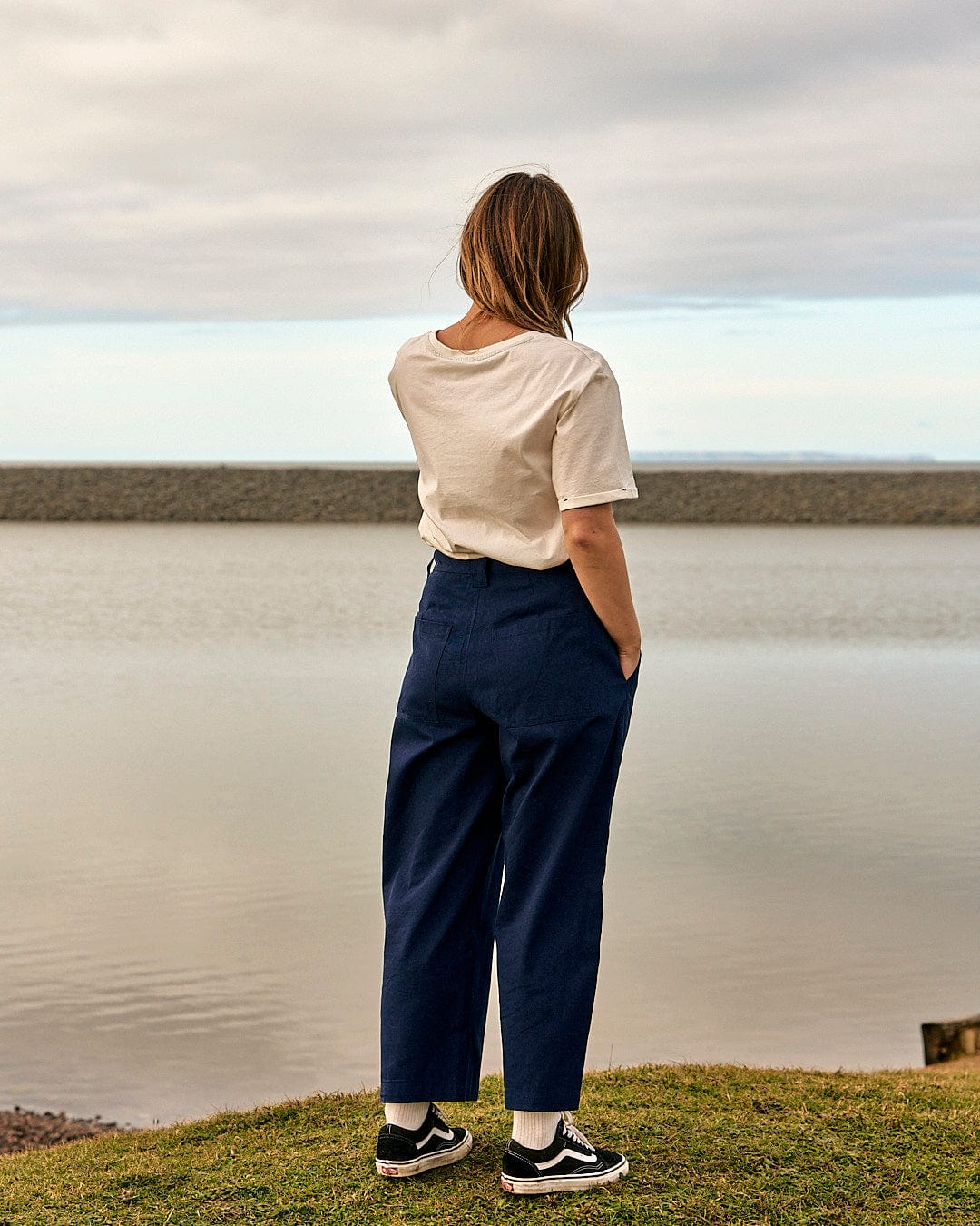 A woman standing by a body of water wearing a Saltrock Hilda - Womens Canvas Trouser - Dark Blue and t-shirt.