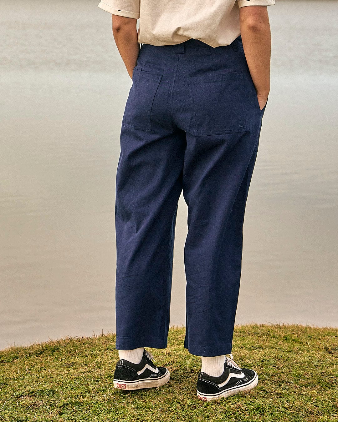 A woman is standing next to a body of water wearing Saltrock's Hilda - Womens Canvas Trouser in Dark Blue.