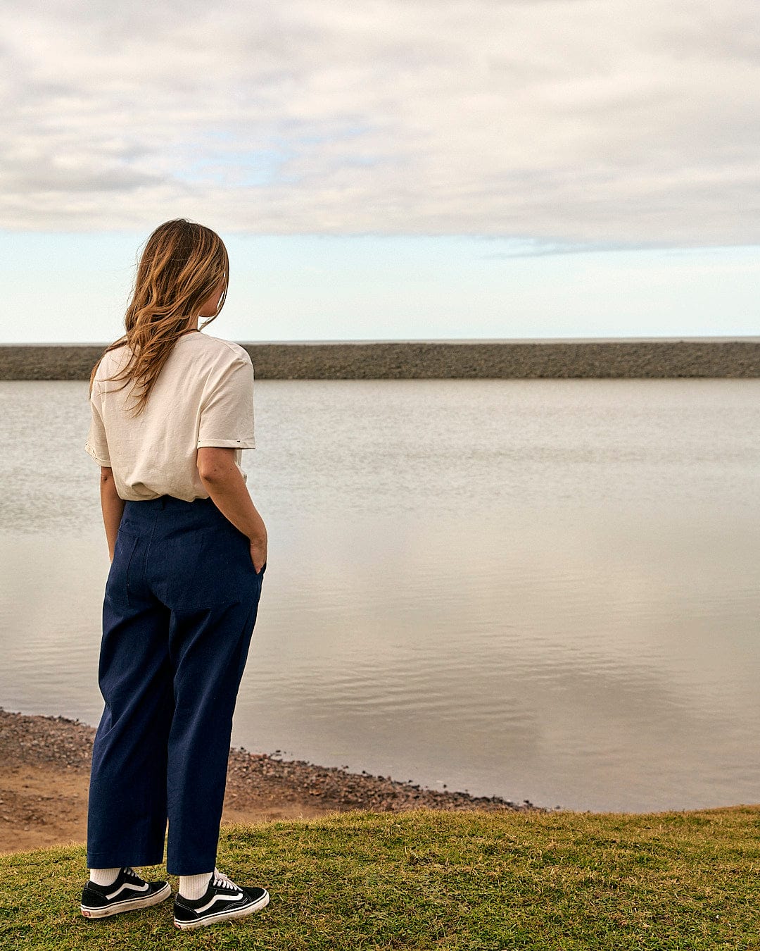 A woman standing in front of a body of water wearing Saltrock's Hilda - Womens Canvas Trouser - Dark Blue.