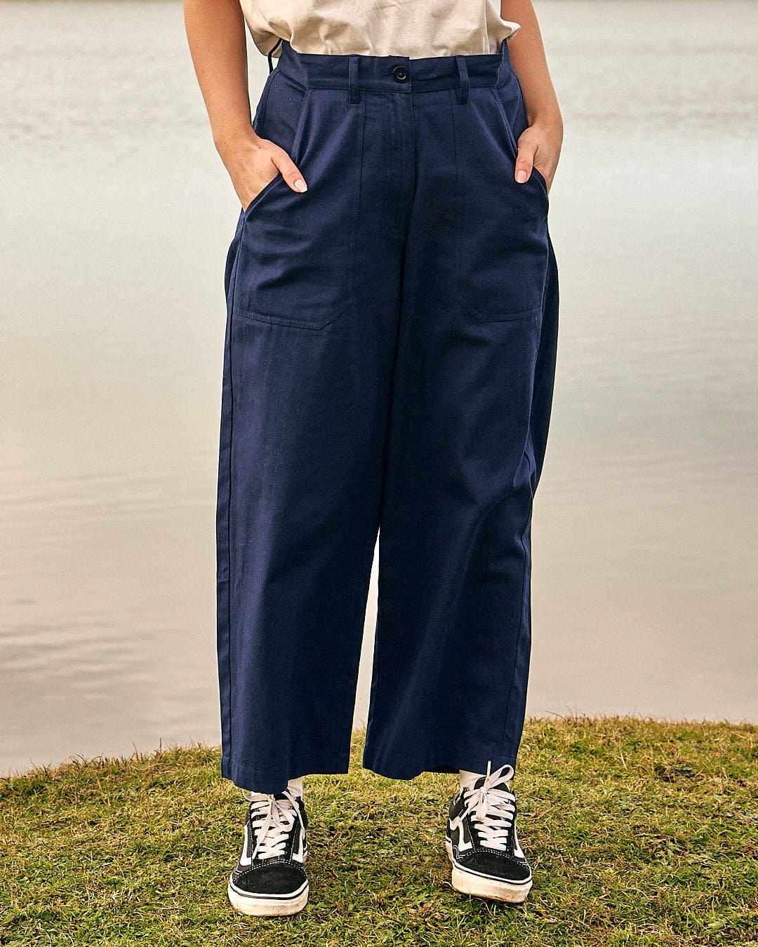 A woman is standing in front of a body of water wearing a pair of Saltrock's Hilda - Womens Canvas Trouser - Dark Blue.