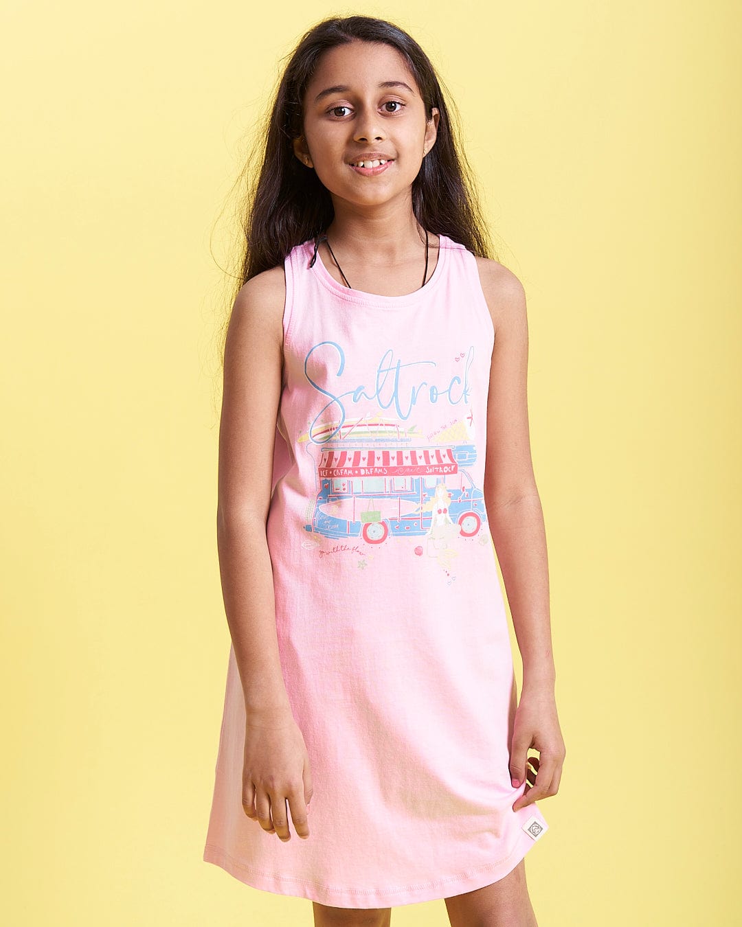 A girl wearing a Ice Cream Dreams - Kids Dress - Light Pink from Saltrock with a truck on it.