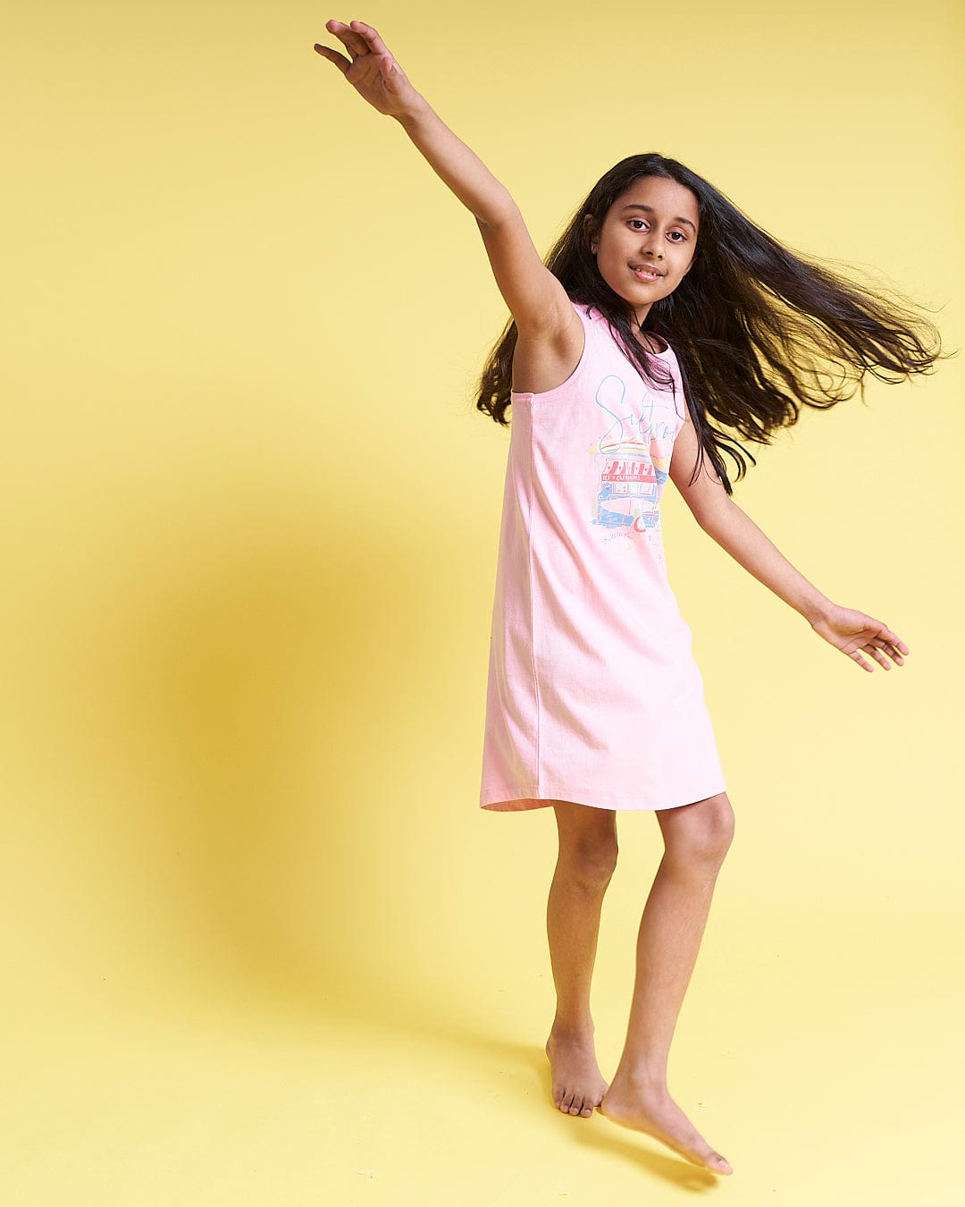 A girl in a Ice Cream Dreams - Kids Dress - Light Pink by Saltrock is dancing on a yellow background.