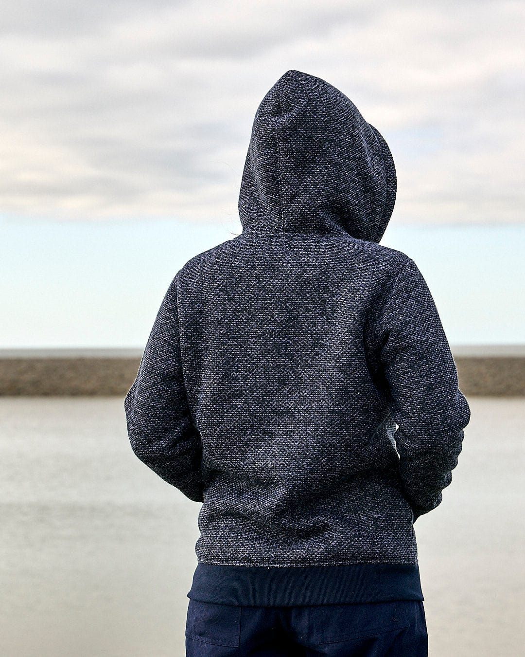 A person wearing a Saltrock - Jazz Womens Borg Lined Zip Hoodie in Dark Blue, looking at the water.