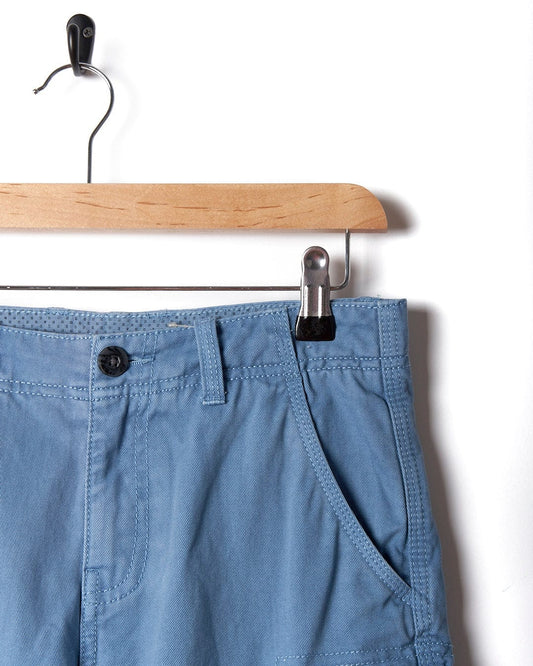 A pair of Saltrock Kaleb - Kids Cargo Short - Light Blue hanging on a hanger.