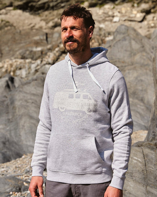 A man wearing a Saltrock hoodie standing on rocks, embracing the Live Life Location - Mens Pop Hoodie - Grey motto.
