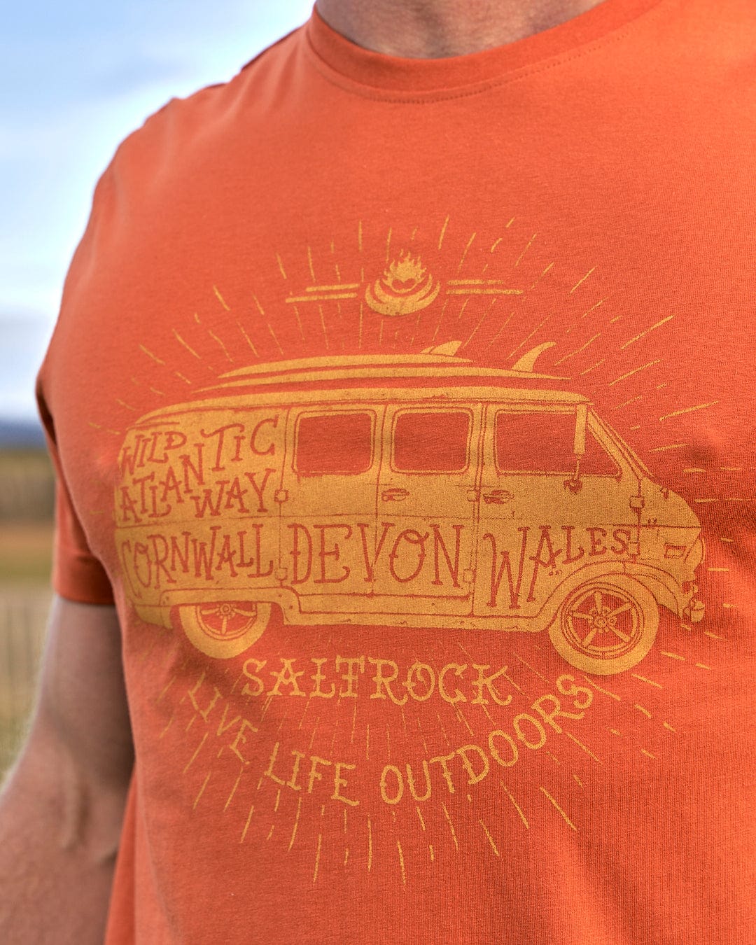 A man wearing a Live Life Location - Mens Short Sleeve T-Shirt - Orange with a van on it by Saltrock.